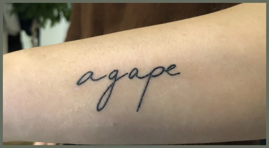 Das Wort agape in feiner Handschrift als Tattoo auf einem Unterarm